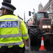 A police officer watches a tractor during a protest by farmers in central London over the changes to inheritance tax (James Manning/PA)